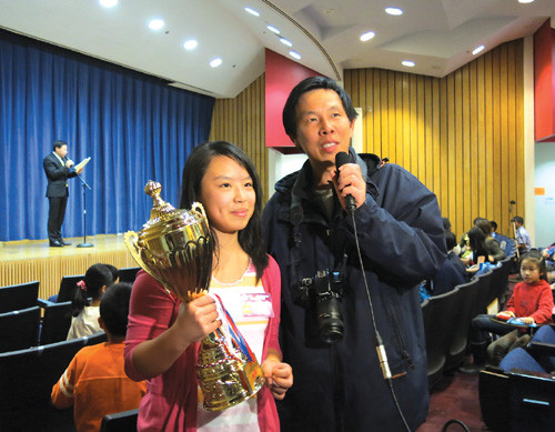 中国侨网捧着奖杯的董语薇和父亲接受采访。（美国《侨报》）