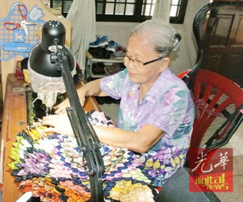李美龄戴着老花镜，踩着老针车，手工制作环保手提袋及地垫。（马来西亚《光华日报》）