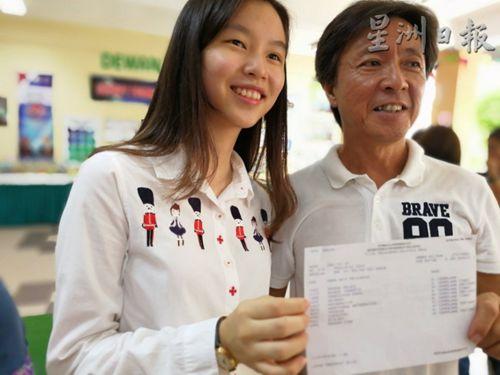 中国侨网王菲莉华文考获A+，与父亲展示成绩单。（马来西亚《星洲日报》）