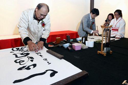 中国侨网马来西亚书艺协会会长王雅（左）在完成作品后盖上姓名印章，于乐（右）专注挥毫。（马来西亚《星洲日报》）