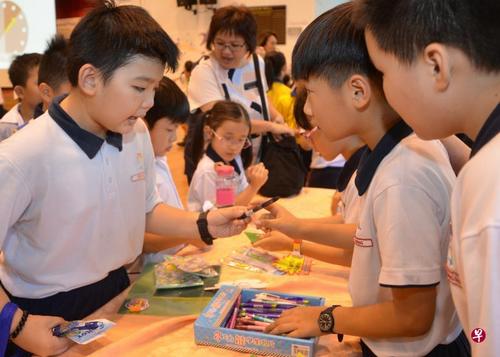 中国侨网光道小学举办的“小小店屋”比赛中，学生以母语“推销”摊位物品，让其他学生用游戏钞票购买，从而鼓励他们实用母语，也灌输基本的创业知识。（新加坡《联合早报》/光道小学提供）