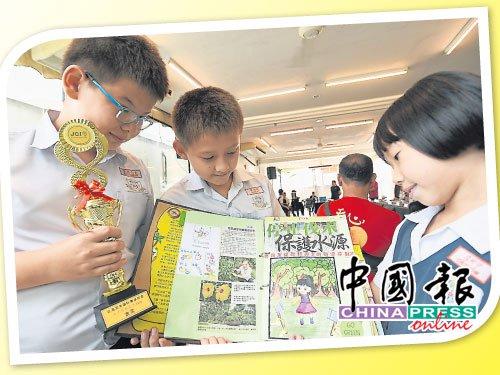 中国侨网文明小学组的亚历山大（左起）、罗柏特及吕珂宁得奖后，展示他们的剪报作品。（马来西亚《中国报》）