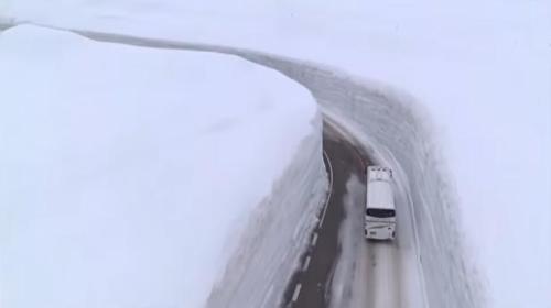 中国侨网资料图:旅游大巴通过高耸的雪墙。(图片来源:立山黑部阿尔卑斯山脉旅游路线官方网站视频截图)