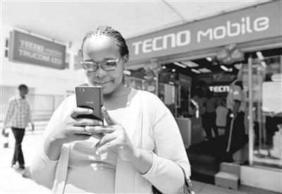 中国侨网在肯尼亚首都内罗毕市中心，一名女子在一家传音手机专卖店前使用自己的传音手机。