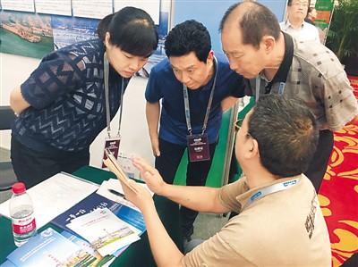 中国侨网在9月14日的郑州项目对接会上,肖文丁(前)向三门峡市的工作人员展示自己在湖北的工厂信息。