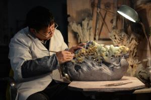 中国侨网非物质文化遗产项目代表性传承人、省级工艺美术大师杜小亮在使用雕刀修细作品