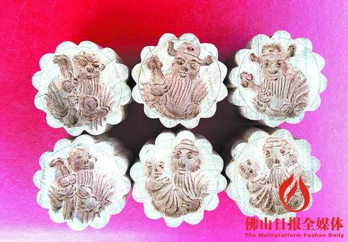 中国侨网佛山饼印传承人杨海成用木材雕刻6个圆柱作品，周边雕有12道齿轮，而面上则刻有“福禄寿”图案，栩栩如生。