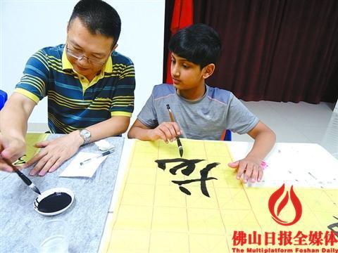 中国侨网禅城兰桂社区,书法老师教来自印度的小男孩龙龙写“龙”字。