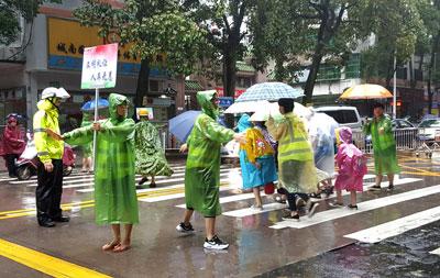 中国侨网护畅队队员冒雨在学校门外维持交通秩序，护送学生进校园。本报记者 庄园摄