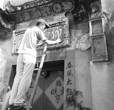 中国侨网郑华在修补门楼上破损的灰雕牌匾。