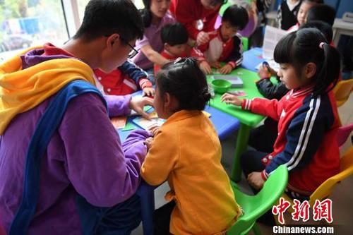 中国侨网4月1日，大学生志愿者和小学生在与自闭症患儿一起学习卡片制作。　张斌　摄