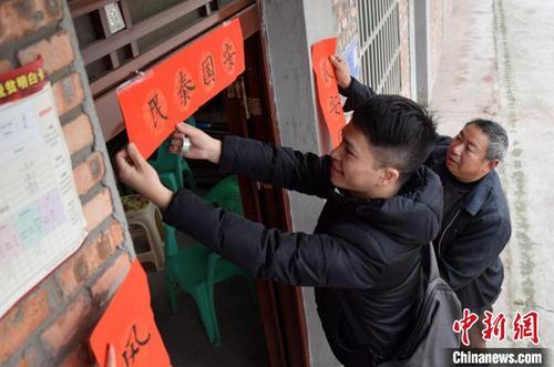 中国侨网扶贫干部为易地扶贫搬迁群众贴春联。　唐明润　摄
