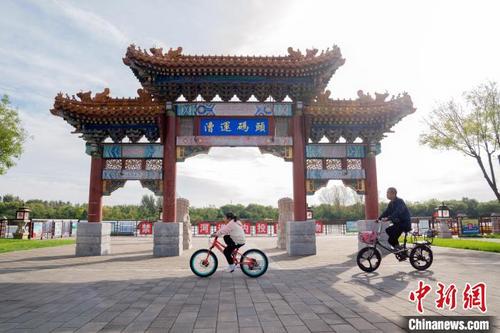 中国侨网北京市通州区运河森林公园，市民骑车经过漕运码头牌坊。　靳秋月　摄