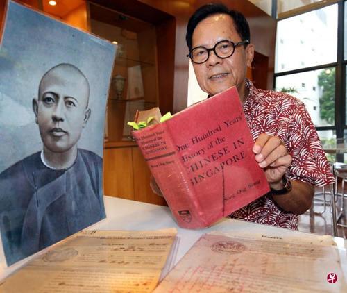中国侨网陈继廉手中的《新加坡华人百年史》是他念大学时买的,至今已有半个世纪。左为其曾祖父陈德源的肖像,桌上摆着陈笃生母亲侯玉娘和陈笃生二哥陈有郎的遗嘱。(新加坡《联合早报》/周柏荣 摄)