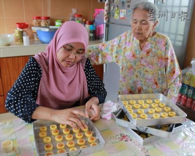中国侨网玛丝丽雅娜的祖母阿尔花（右）年届80岁高龄，平时喜欢看孙女在厨房制作糕饼。（马来西亚《星洲日报》）