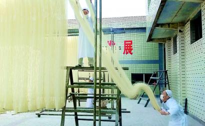 中国侨网合什手工面的传承人正将发酵后的面条,晾晒在2米多高的木架上,拉伸成细如发丝的手工面。