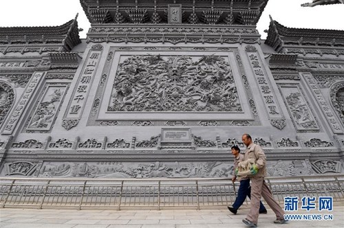 10月16日，沈占伟(右)从他和徒弟们历时两年、精雕细刻数千块青砖组合而成的九龙壁下走过。新华社记者