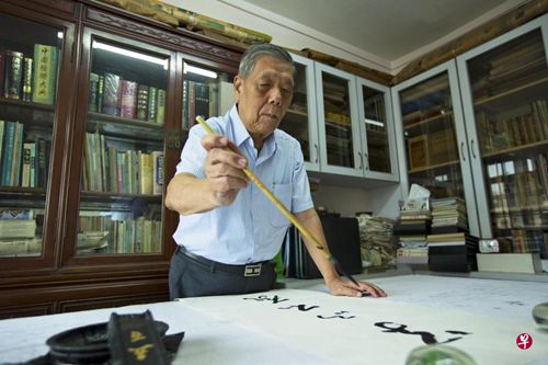 中国侨网70多年来不离笔砚的曾守荫,写书法时坚持用研磨出来的墨汁。这是他在书房写字的情景。(新加坡《联合早报》/曾道明摄)