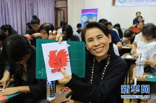 中国侨网22日,曼谷市教育局副局长塔妮达在活动现场展示自己的“雄鸡”剪纸作品。