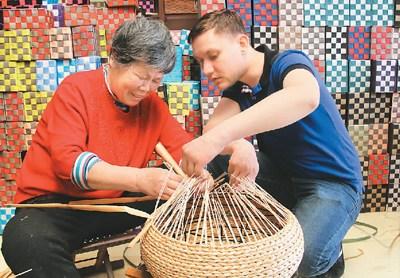 中国侨网图为4月15日，来自摩尔多瓦的比契尔(右)在农民梁春梅(左)指导下体验草柳编工艺品编织技艺。（陈彬 摄）