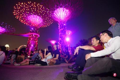 中国侨网王乙康部长与滨海湾花园运营总监罗志威（右）与民众席地而坐，观赏“花园狂想曲”这个灯与音乐的盛宴。（新加坡《联合早报》/梁伟康 摄）