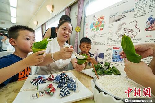 中国侨网一名乘务员教小朋友包粽子。 中新社记者 贺俊怡 摄