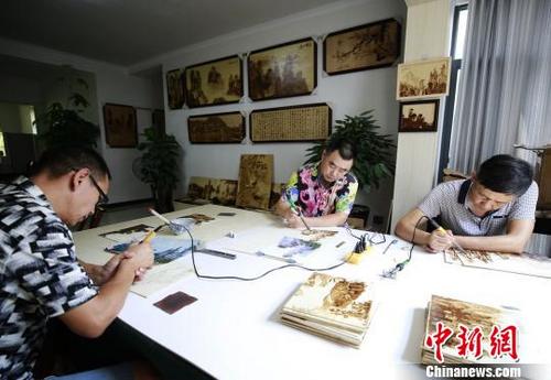 中国侨网邓师华（中）和他的团队用烙铁绘制张家界山水画。　吴勇兵　摄