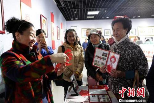 中国侨网市民孙仙梅展示肖像剪纸并与伏兆娥互动。　胡耀荣　摄