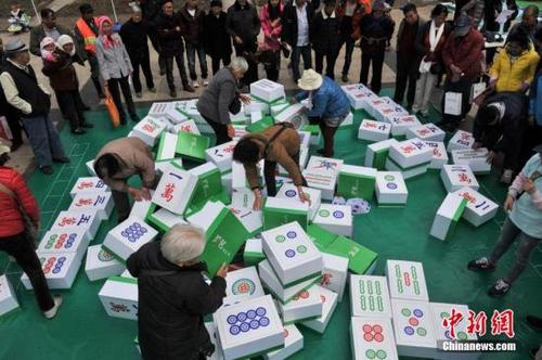 中国侨网资料图:昆明一商家在街头摆出“巨型麻将”,规则是第一个组成胡牌的队伍为胜,吸引市民对阵切磋。图为市民在麻将堆里选牌。 中新社记者 任东 摄