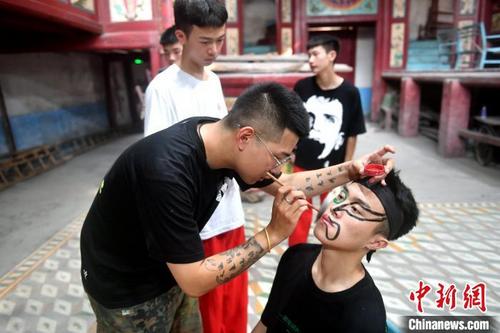 中国侨网福州锦麟轩八将团团长黄杜飞正在给“00后”团员画脸谱。 吕明 摄