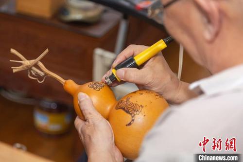 中国侨网9月29日下午，刘振在自己家中手拿电烙笔在葫芦上进行创作。　刘力鑫　摄