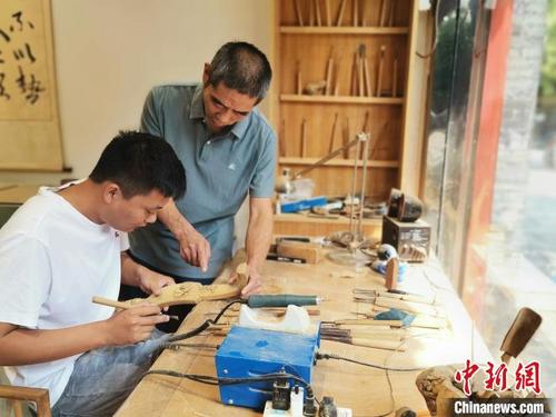 中国侨网在山东曲阜孔庙附近的一家手工店,楷雕非遗传承人张利生正在指点自己的徒弟雕刻如意。 赵晓 摄