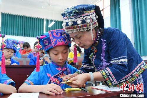 中国侨网图为仫佬族剪纸技艺传承人罗华清在指导学生学习仫佬族剪纸技艺。　廖光福　摄