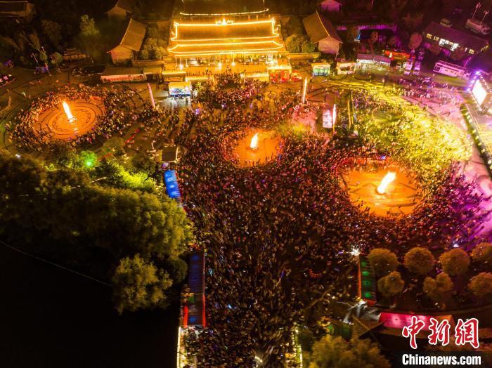 中国侨网8月10日，2024年贵州省毕节市“自然凉·毕燃嗨”火把狂欢暨避暑旅游季的压轴大戏之“和美之夜”在大方县拉开帷幕，当晚举行的篝火狂欢活动吸引众多游客前来游玩体验，感受当地独特的民族风情和地方文化。图为游客在毕节市大方县宣慰府参加篝火狂欢活动。罗大富 摄