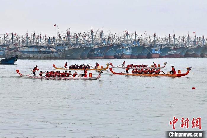 中国侨网6月5日，中国传统端午节临近，福建省晋江市海上龙舟公开赛在深沪镇渔业码头开赛，12支海内外龙舟代表队一同在深沪湾竞速。图为比赛中的龙舟经过一排排渔船。王东明 摄