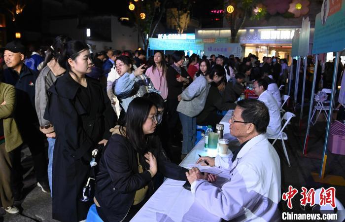 10月24日,安徽省黄山市屯溪区黎阳水街举办“新安岐黄夜·康养在黄山”中医夜市活动,现场医护人员变身“夜市摊主”,展示把脉、推拿、针灸、刮痧、火龙灸等技艺,免费为民众提供健康咨询和诊疗服务。图为中医医师为市民把脉问诊。中新社记者 韩苏原 摄