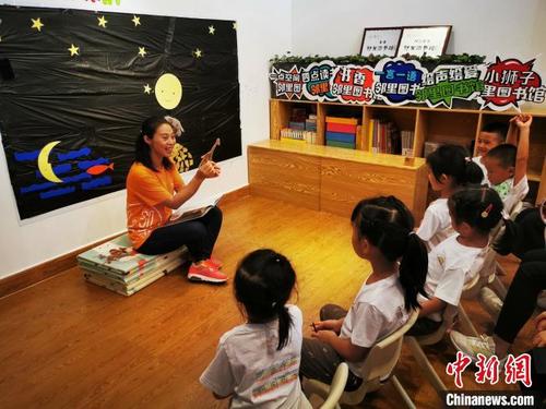 中国侨网四点读书邻里图书馆馆长王丽琴正在带领孩子们读绘本《月亮的味道》。　应妮　摄