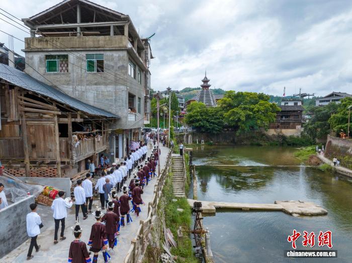 中国侨网2025年8月7日是贵州省黔东南苗族侗族自治州从江县西山镇顶洞村一年一度新米节,也是当地侗族的成人礼。全村即将迈入成人行列的少男少女,身着节日盛装,欢聚于鼓楼与风雨桥之间,吟唱着悠扬的侗歌,向先祖虔诚地宣告自己的成年,期盼着在爱情的田野上自由驰骋,在事业的征途上勇敢前行,祈福得到先祖的保佑。图为顶洞村的侗族少男少女前往鼓楼准备参加成人礼。(无人机照片)吴德军 摄