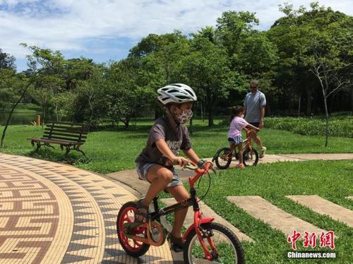 中国侨网资料图：巴西圣保罗，一名儿童戴着口罩在当地一公园骑车锻炼。 中新社记者 莫成雄 摄