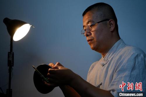 中国侨网在白炽灯光的映照下，身着中山装、戴着老花镜的郭智军正坐在工作台前利用锔瓷技艺修复一只破碎的黑釉碗。　韦亮　摄