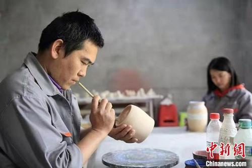 中国侨网张俊良正在对陶艺产品绘制。　受访者提供。
